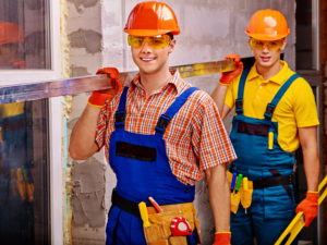 two commercial contractors smiling and holding a wooden plank