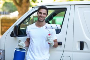 happy commercial painter holding roller and paint standing in front of his white van