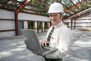 commercial contractor with a laptop and hardhat on standing on a semi built location