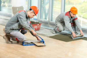 two construction workers installing carpet floors in a room with large windows