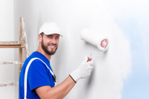 happy painter wearing a blue shirt and white suspenders painting the interior of a home white