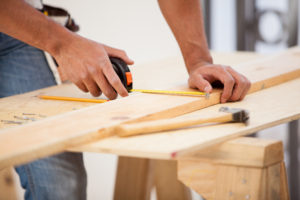 general contractor using a tape measure to check a plank of wood