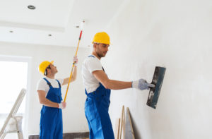 two professional painters painting a home's bedroom with paint rollers 