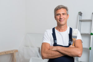 professional painter smiling with arms crossed and a paint brush in ahnd