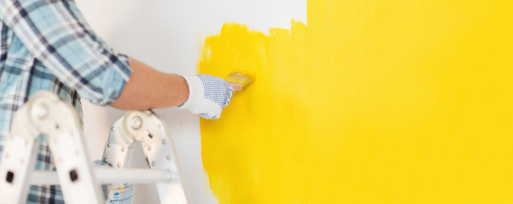 a worker doing painting remodeling on a home with yellow paint 