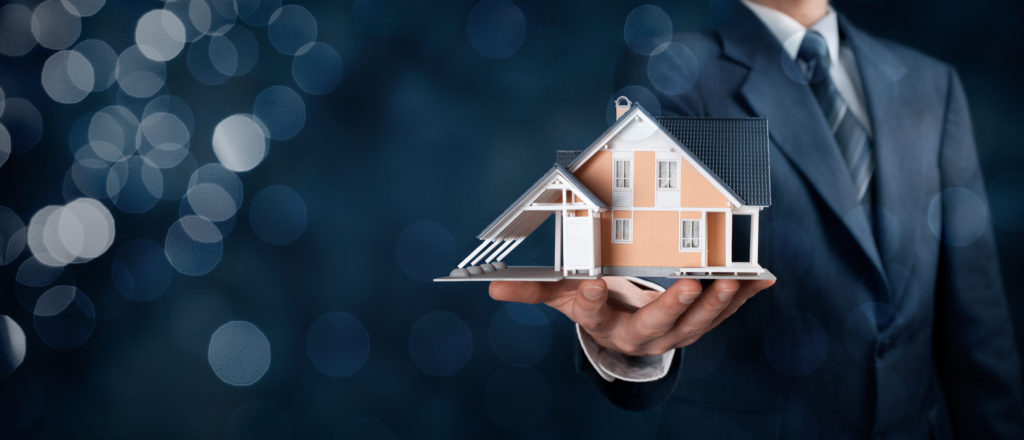 a man holding a model of a home in the palm of his hand