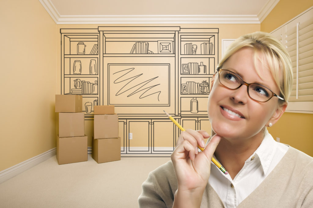 Daydreaming woman holding a pencil In empty room with a concept drawing for remodeling on the wall